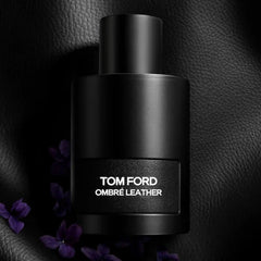 Black Tom Ford Ombre Leather perfume bottle on a dark textured background with purple flowers.